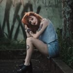 Stylish redhead woman with tattoos posing outdoors with graffiti backdrop.
